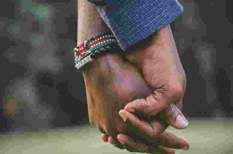 Two people holding hands outdoors, one wearing beaded bracelets.