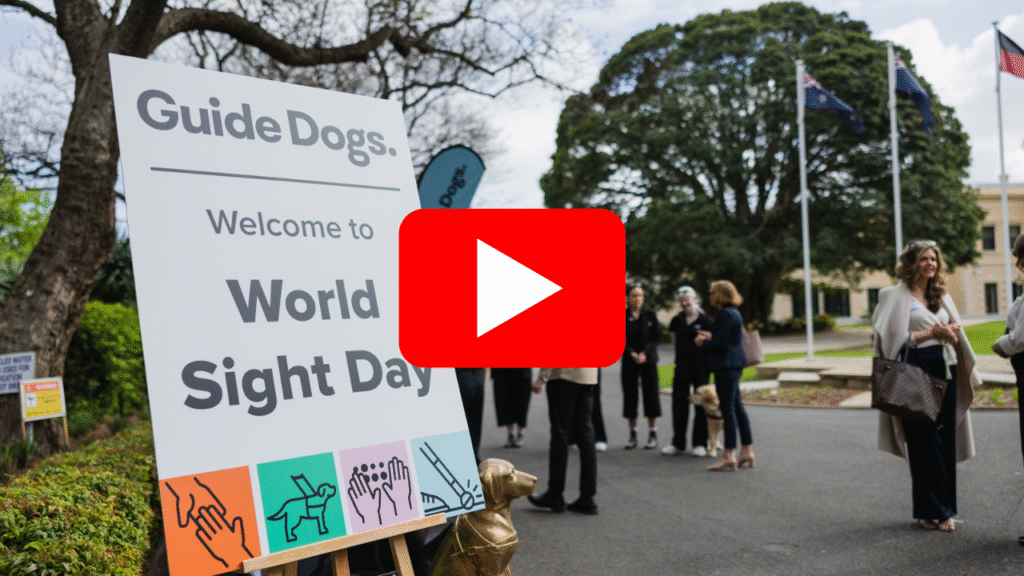A large sign reads Guide Dogs. Welcome to World Sight Day at an outdoor event with people gathered in the background.