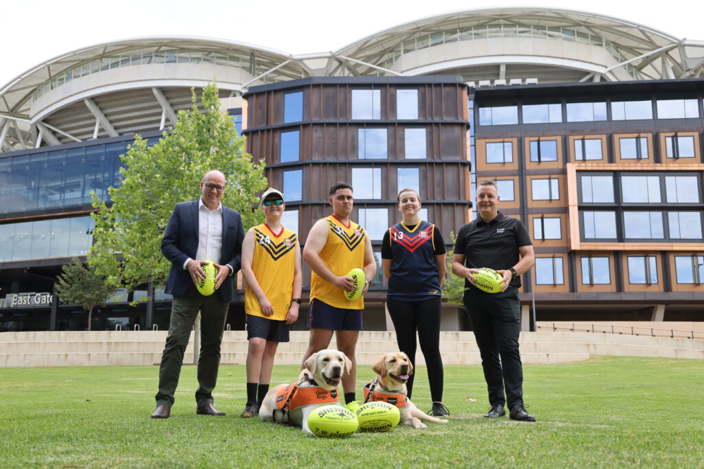 Pictured from left, SANFL Head of Game Development Brad Humphrey, Blind Low Vision participants Isaac McInnes, Tyreece Bevan and Amelia Hart and Guide Dogs SA/NT Chief Operating Officer Jason Clark with Guide Dogs Merlin and Tofu.