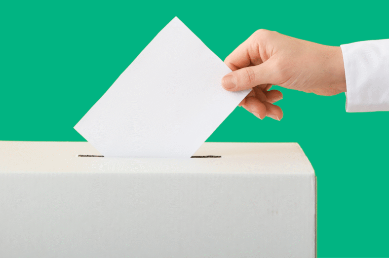 A hand places a white envelope into a slot on a white box against a green background.