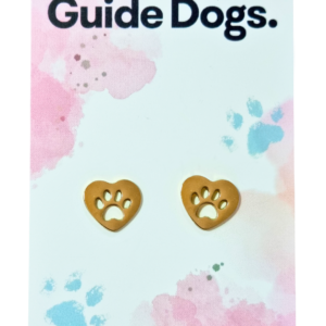 Earrings - Heart: Gold heart-shaped stud earrings with paw print cutouts, displayed on a card with pastel paw prints and the message "Proudly supporting Guide Dogs.