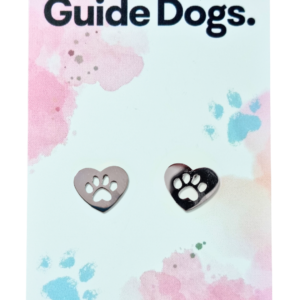 A pair of Heart earrings made from stainless steel with paw print cutouts, presented on a card stating “Proudly supporting Guide Dogs.”.