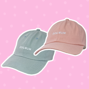 Two Caps, one light blue and one light pink, both with "DOG MUM" embroidered in white, displayed on a pink polka dot background.