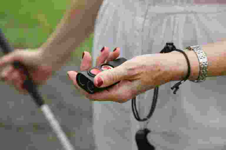 Person standing outside with a white cane in one hand and a Miniguide in the other.