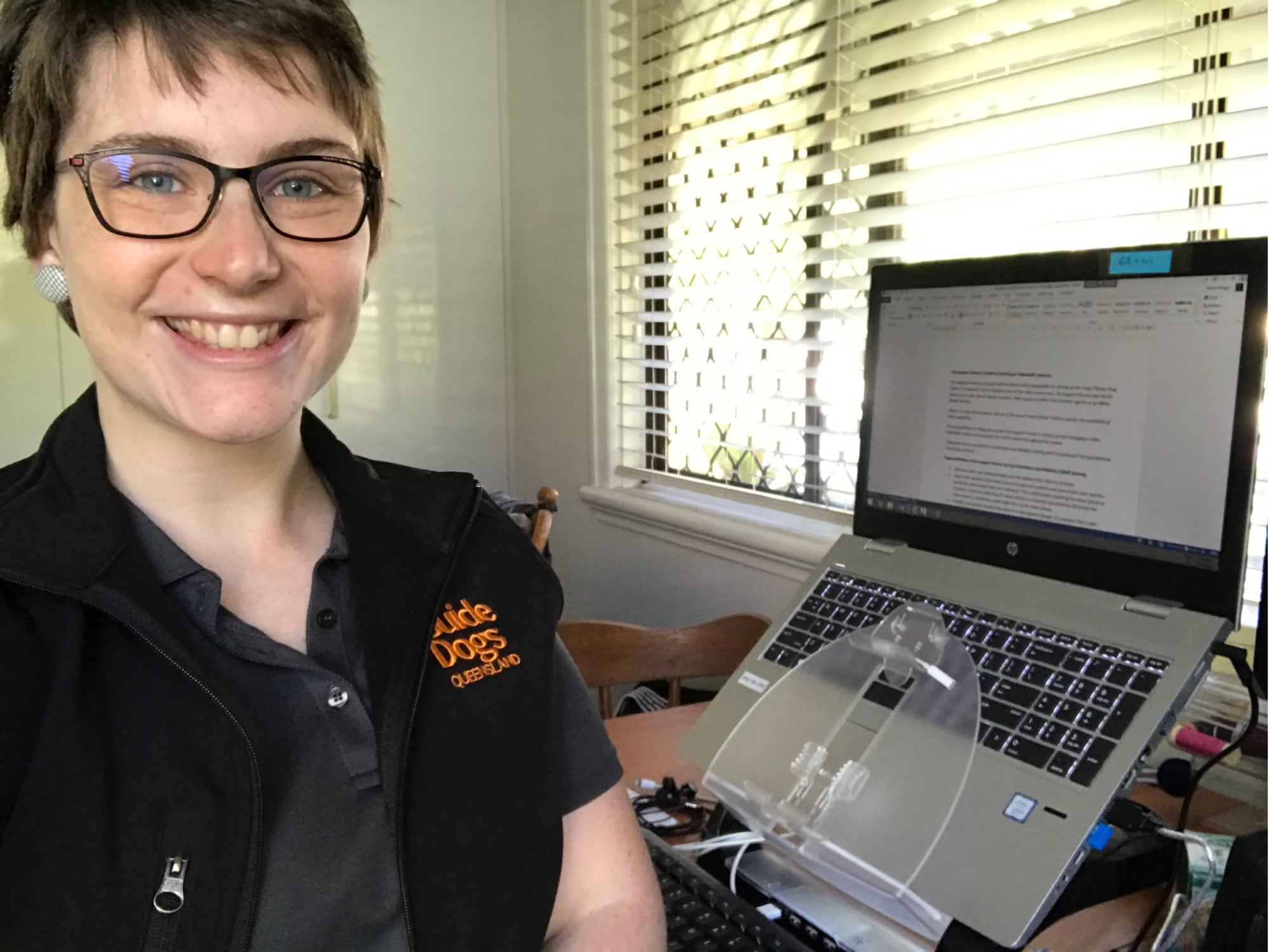 A Guide Dog's staff member sitting at a laptop. The staff member is looking at the camera smiling