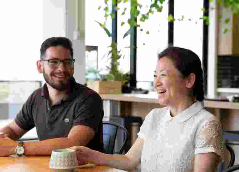 Two people sitting at cafe table. Both people are smiling.