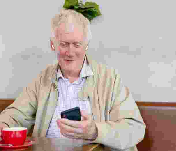 An older adult man sitting at a cafe looking at their phone.