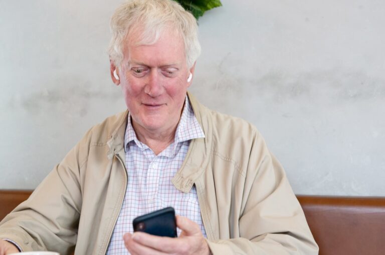 An older adult man sitting at a cafe looking at their phone.