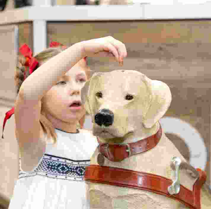 A young child putting a coin into a large Guide Dogs collection dog.