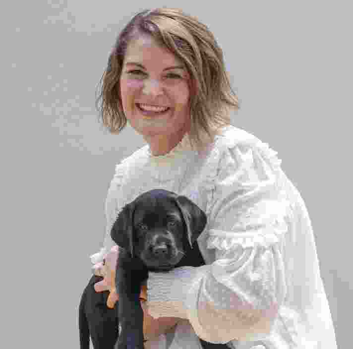 Guide Dogs staff members holding black labrador puppy and smiling at the camera.