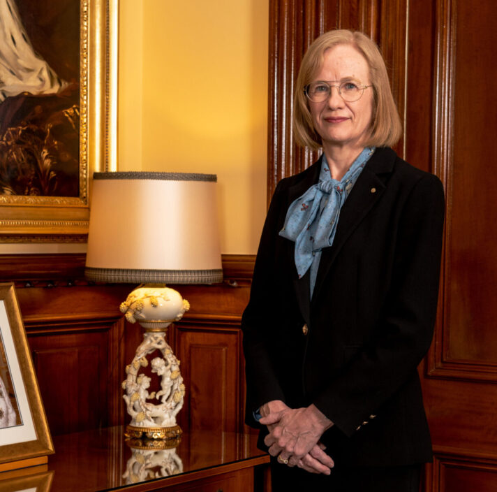 Her Excellency the Honourable Dr Jeannette Young PSM Governor of Queensland standing next to a side table with a framed photo of Her Majesty Queen Elizabeth II