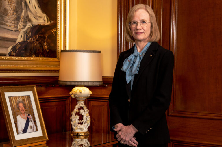 Her Excellency the Honourable Dr Jeannette Young PSM Governor of Queensland standing next to a side table with a framed photo of Her Majesty Queen Elizabeth II