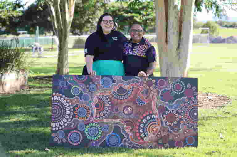 Client Services team member Sarah stands with artist Laurie Anno and the artwork he presented to Guide Dogs Queensland.
