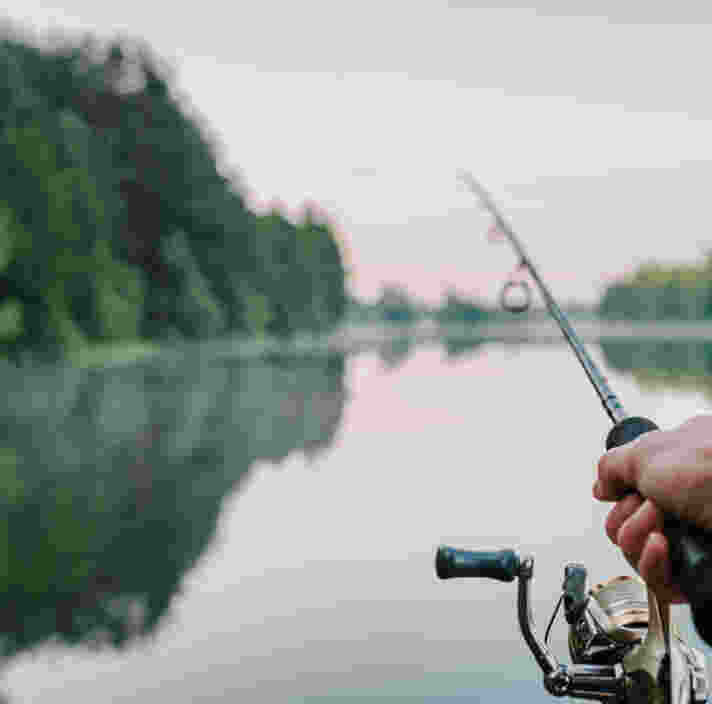 a hand holding a fishing reel in front of a lake