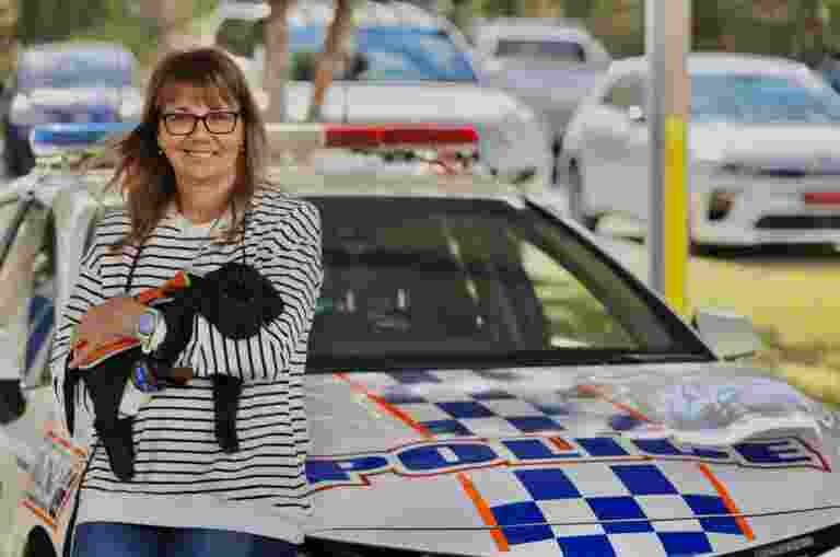 A woman holding Davey, a black Labrador puppy, in her arms. She is standing in front of a police car.