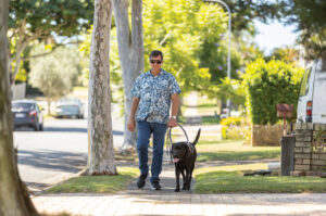 Image of Jason and Guide Dog Tyson walking down a street on the footpath.