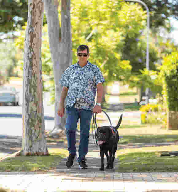 Image of Jason and Guide Dog Tyson walking down a street on the footpath.