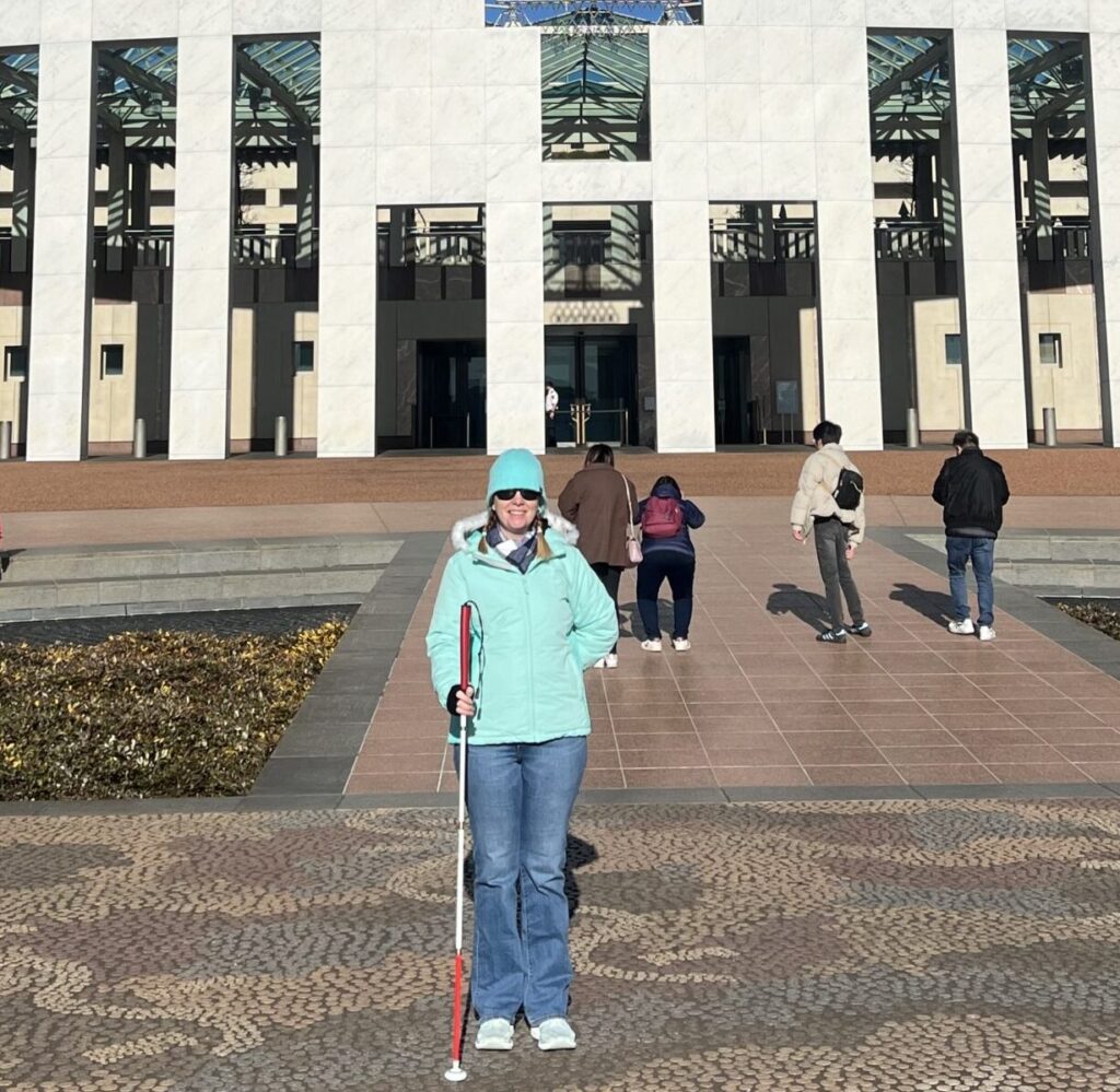 Pictured right, Sarah is standing with her white cane in front of Parliament House, Canberra.