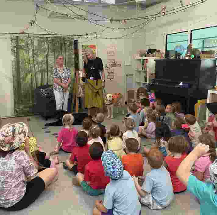 A group of children listening sitting in a class listening to someone speak.