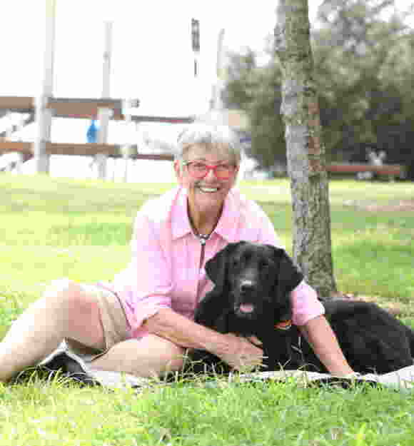 Sue and Guide Dog Vegas sitting on the grass smiling at the camera.
