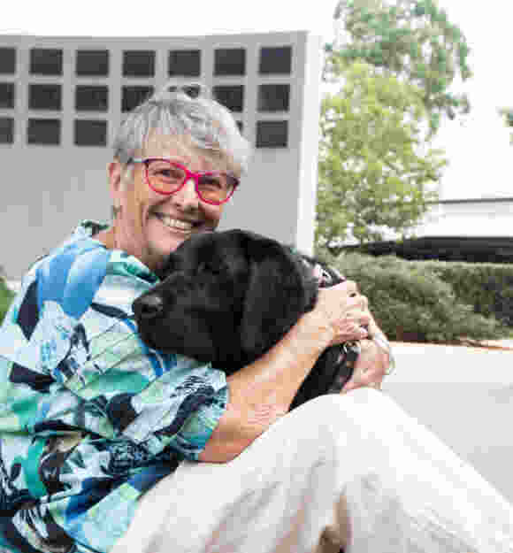 Sue cuddling Guide Dog Vegas while sitting on the ground.