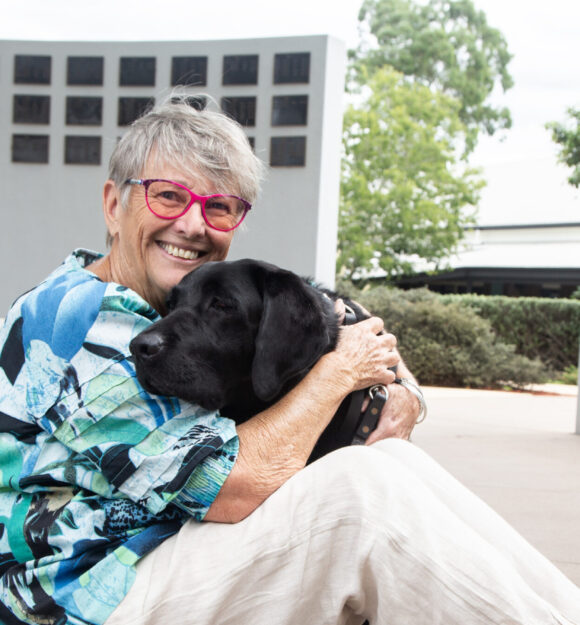 Sue cuddling Guide Dog Vegas while sitting on the ground.