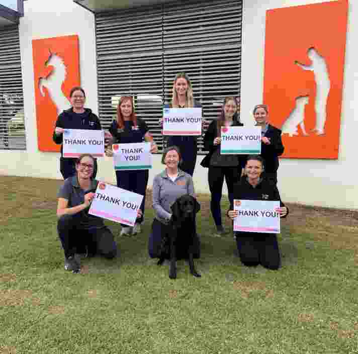 Seven Guide Dogs staff members sit on some grass holding Thank you signs.
