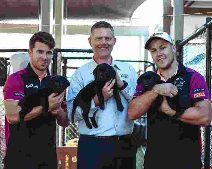 Three people stand holding puppies in the Guide Dogs Nursery.