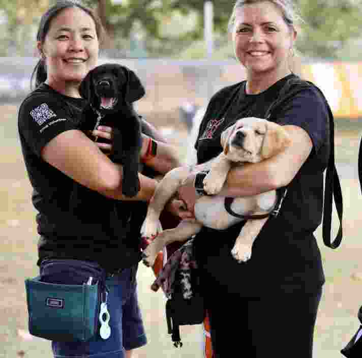 Two Guide Dogs team members holding puppies.