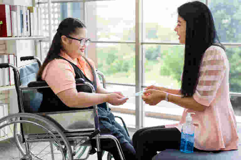 A psychologist is pictured holding out a card to young girl wearing glasses in a wheelchair.