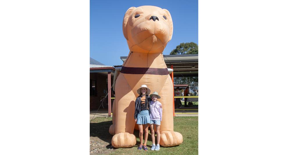 Two girls are standing in front of a giant inflatable Guide Dog and smiling at the camera.