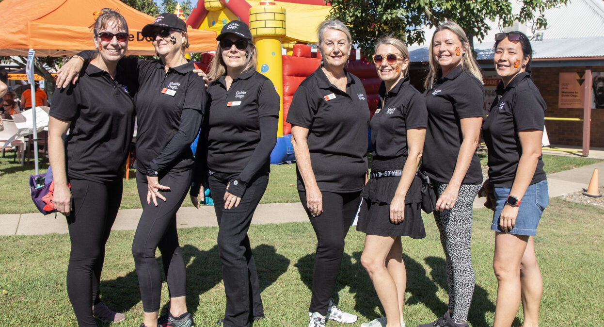A group of Guide Dogs staff are standing in a row and smiling at the camera. The staff have paw prints facepainted on their cheek.