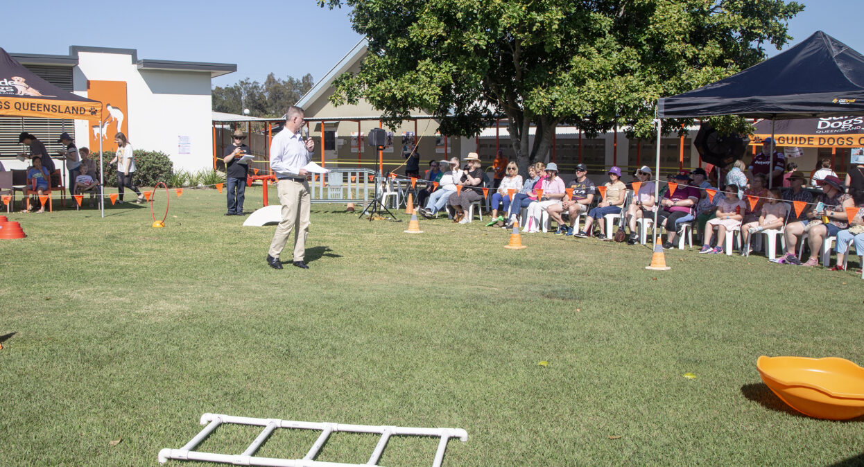 Guide Dogs CEO Jock Beveridge standing in an arena with obstacles is speaking to a crowd of spectators.