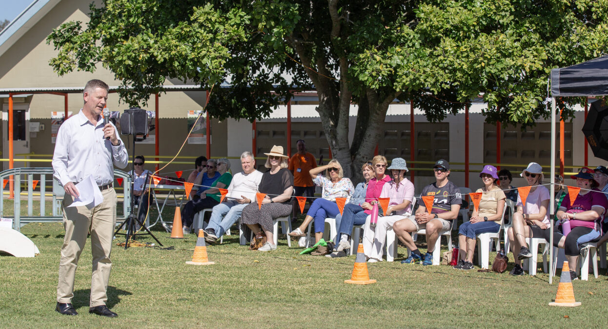Guide Dogs CEO Jock Beveridge standing in an arena with a microphone speaking to a crowd of spectators.