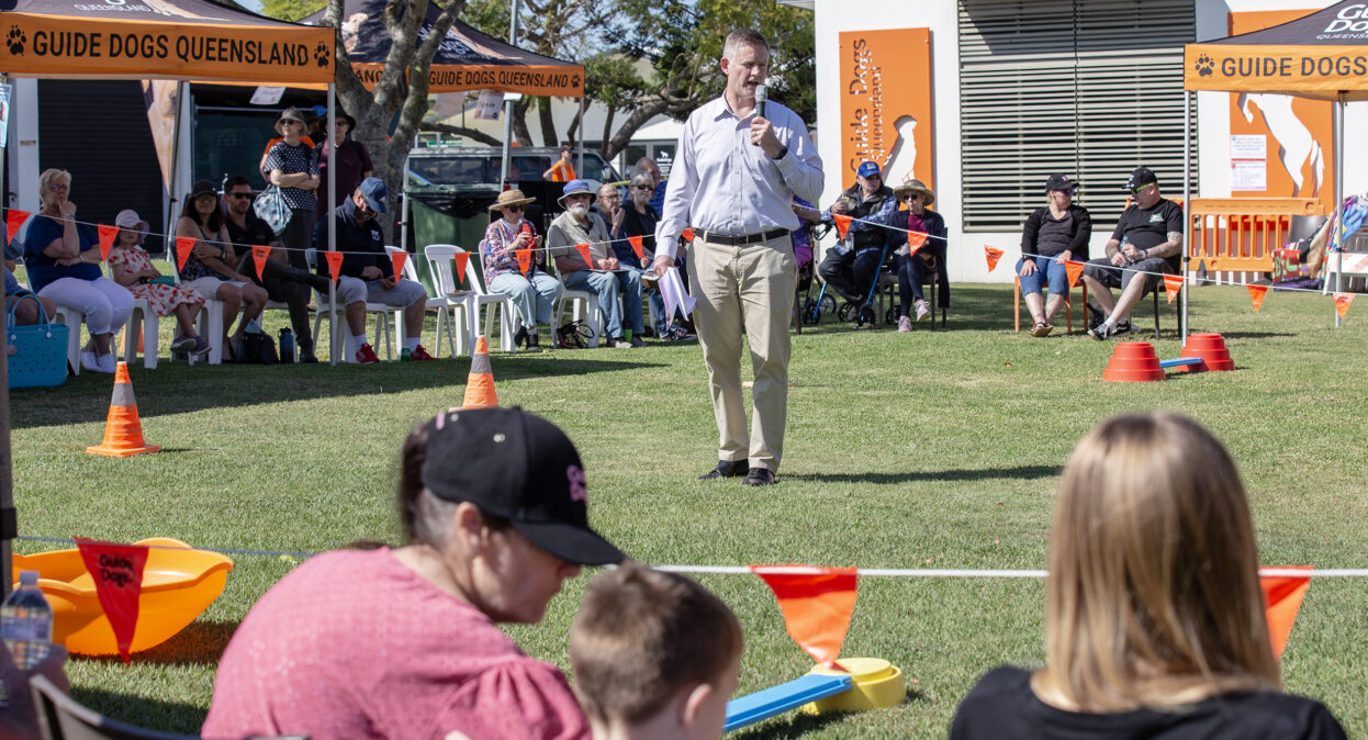 Guide Dogs CEO Jock Beveridge standing in an arena with a microphone speaking to a crowd of spectators.