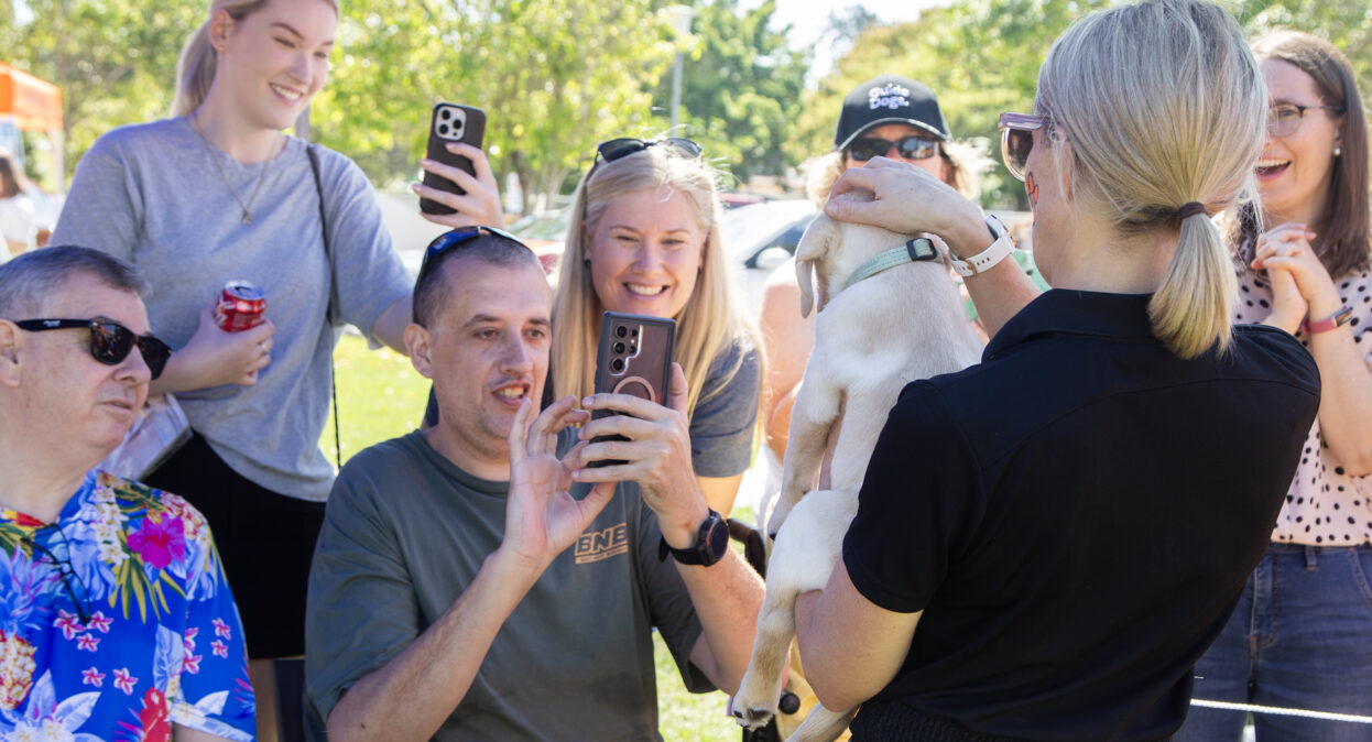 A puppy trainer holding a yellow Labrador puppy as a group of people take photos of the puppy on their phones.