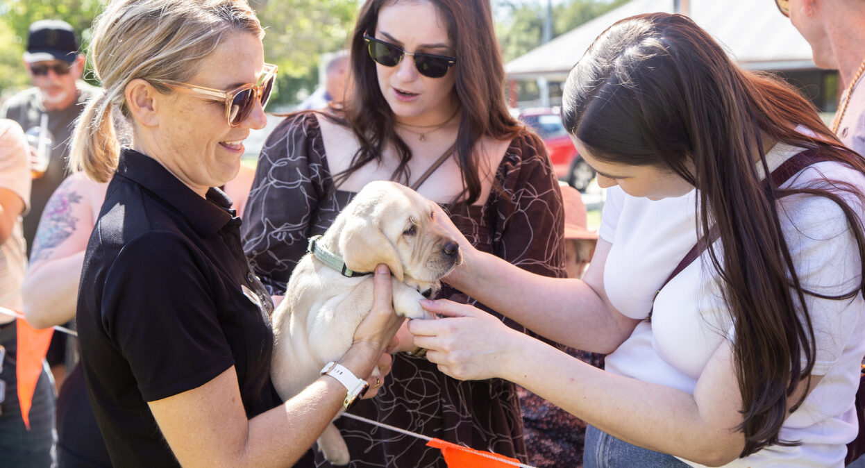 A puppy trainer holding a yellow Labrador puppy as a two ladies pat the puppy.