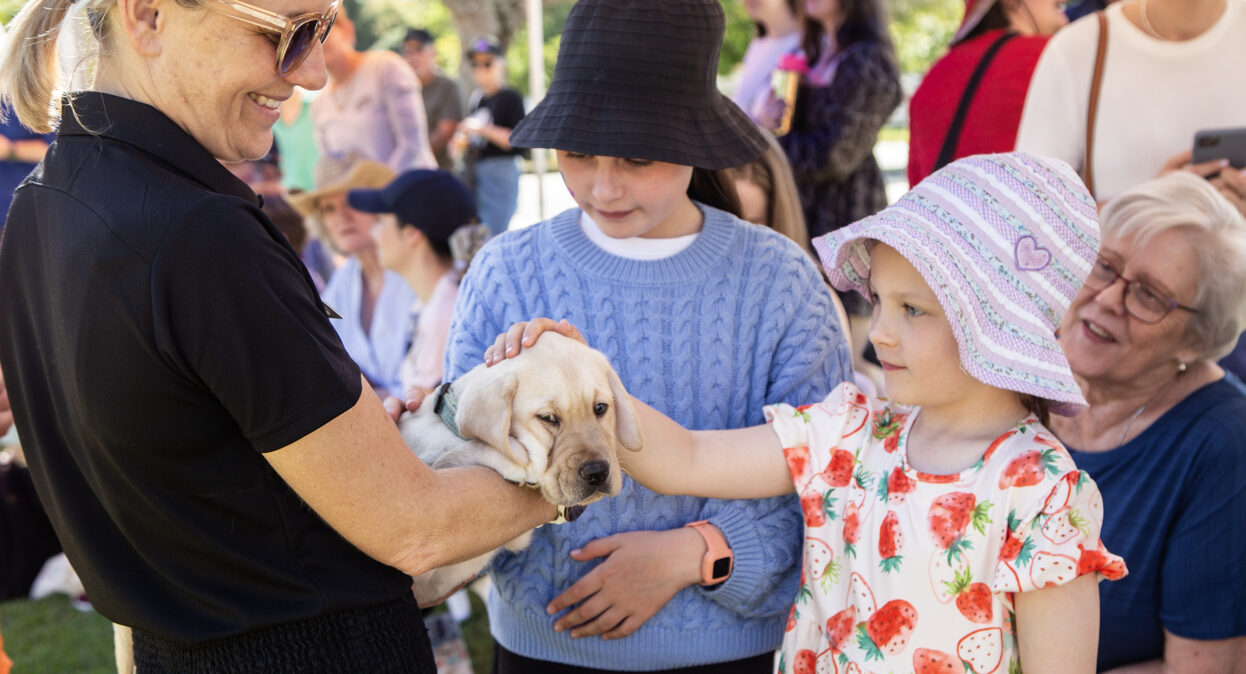 A puppy trainer holding a yellow Labrador puppy as a two young girls pat the puppy.
