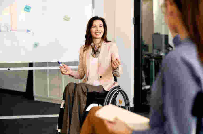 A business woman in a wheelchair is pictured presenting in front of a whiteboard