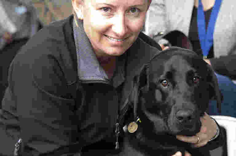 Jodie is pictured smiling to camera next to a black Labrador Guide Dog named Phil.
