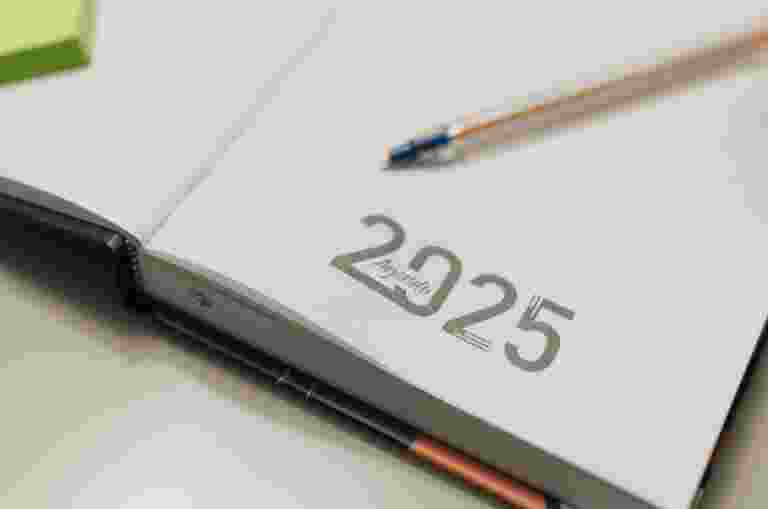 A date diary lays open with the text '2025' on the page. A pen lays above it.