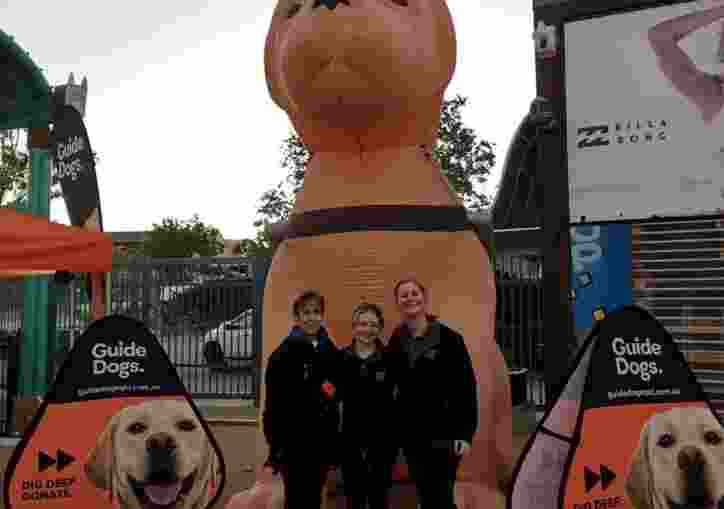 Three people standing in front of a large inflatable yellow Labrador.