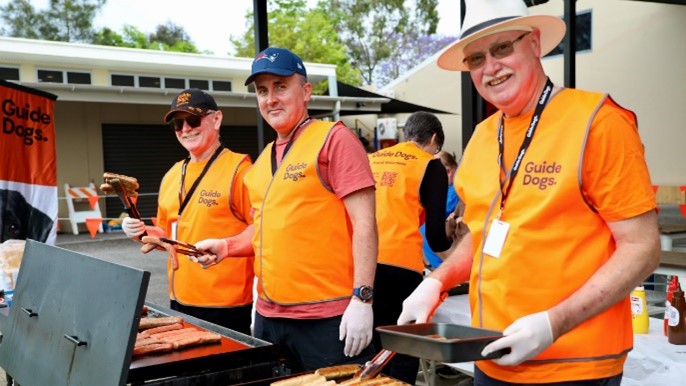 Image shows three volunteers cooking at a BBQ wearing Guide Dogs vests.