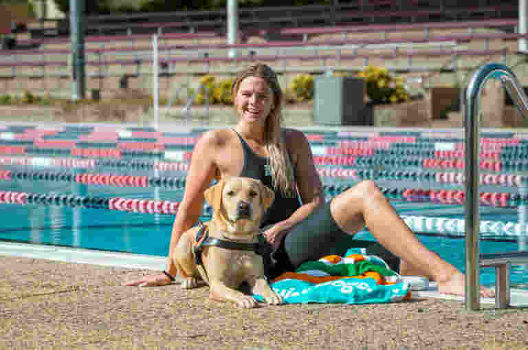 Image shows Australian swimmer Shayna Jack smiling by a swimming pool with a guide dog at her side, highlighting her new role with Guide Dogs Queensland.