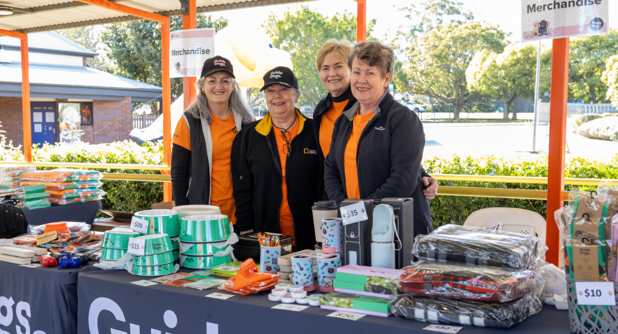 Image shows volunteers in front of a Guide Dogs merch stall.