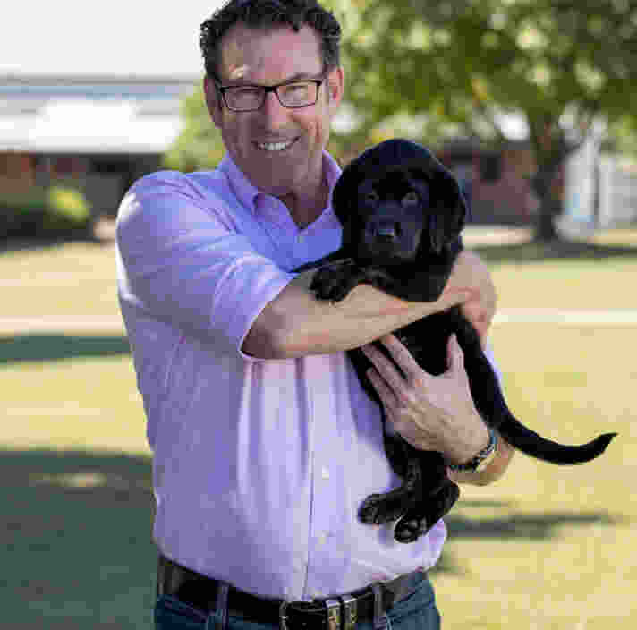 Greg smiling at the camera holding a labrador puppy.