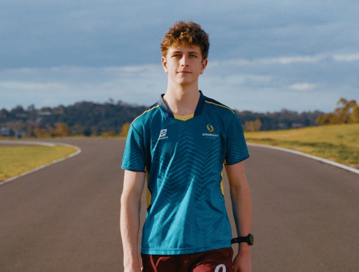 Image shows Mitchell in a teal athletic shirt standing on a curved running track