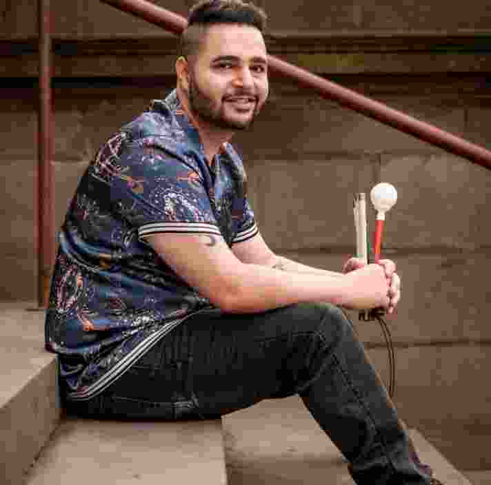 Guide Dogs staff member Karan Nagrani sitting on steps outside holding his white cane.